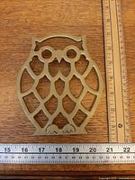 Front view of brass owl trivet with ruler for scale