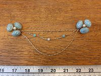 Front view showing both cluster pins, draped chains and ruler for scale