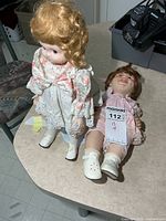 Both porcelain dolls on tabletop showing sizes and outfits