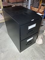 Front view of black 2-drawer Staples file cabinet showing label holders, handles, lock