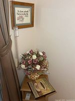 Corner setup showing needlepoint on wall, floral basket and plaques on table