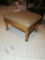 Oblique view showing full stool, wooden frame, turned legs, tan cushion