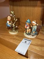 Both Hummel figurines on shelf with lot tag