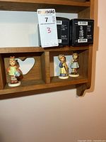 Shelf with three Hummel figurines and two boxes visible