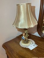 Whole lamp on table showing shade, base with Hummel figure