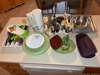 Countertop view showing majority of lot including cutlery, utensils, salad spinner, dish rack, immersion blender, can opener, mixing bowl, broiler pan, purple steamer