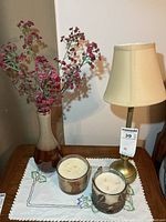 Lamp, vase with flowers, two candles on embroidered mat