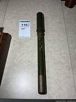 Full view of telescope showing olive body and brown eyepiece, length reference with lot tag