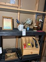 Wide view of shelf showing framed print, white mug with pens, artificial flowers, ceramic mug with floral, black three-hole punch, small framed print, brown cylindrical case, wooden organizer