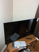 Front view of Samsung 43" LED TV on stand with remotes and manual visible