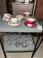Full lot showing teacups, saucers on top shelf and assorted glassware on lower shelf