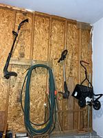 Overview of lawn seeder, two trimmers, hose and bamboo stakes hanging on wall