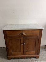 Front view of wooden commode with marble top, drawer, and cabinet doors