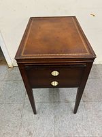 Front view of end table showing leather top, two drawers, brass pulls, legs