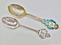 Top view of both spoons showing engraved bowls, enamel crests, handle patterns, gold wash on larger spoon