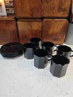 Full set of 6 black octagonal mugs and 6 saucers displayed