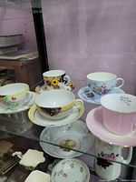 Five assorted teacup and saucer sets displayed in cabinet