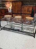 front view of three glass jars in metal rack with cork lids