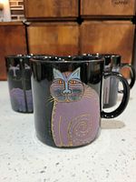 Front view of mug with single purple cat; other two mugs visible behind