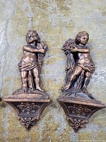 Two cherub wall plaques close-up showing bronze finish and shelf detail