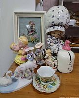 Group shot of all ceramic and porcelain child-themed items including cookie jar, piggy bank, figurines, swan, unicorn, teacup, saucer and framed embroidery