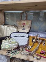 Shelf view showing straw tote, metallic bag, quilted pouch, satin bag, jewelry box and costume necklaces