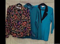 Three garments on hangers: paisley blouse, teal jacket, teal blazer