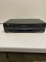 Front view of powered-on JVC HR-VP648U VCR showing display and front inputs
