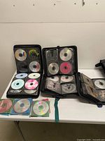 Three open CD organizer wallets and four jewel-case CDs displayed on table