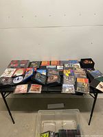 Tabletop overview of mixed DVDs and music CDs on folding table with additional discs in bin below
