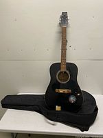 Full view of black acoustic guitar standing on padded gig bag
