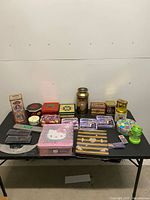 Full table view of mixed tins, jars, pencil sets, and novelty items