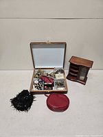 Overall lot showing wood jewelry box open with contents, mini cabinet, red case, black accessory