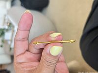Gold-tone arrow collar bar clip held between fingers
