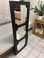 Full view of black painted wood framed triple mirror leaning on bench