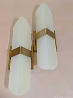 Two identical gold and frosted glass wall sconces shown side by side