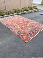 Full view of red Turkish rug unrolled on driveway