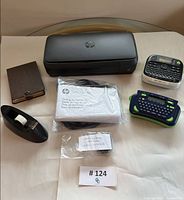 Top-down view of all items: HP printer, two label makers, tape dispenser, planner, cables and manuals