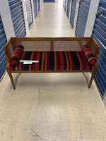 Front view of wooden cane-back bench with striped upholstery and two bolster pillows