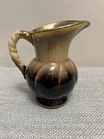 Side view of ceramic drip glaze pitcher showing body, handle, base