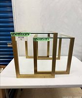 Front view of both nesting tables showing burnt-gold frames and glass tops