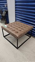 Full view of square ottoman showing tufted top and metal base