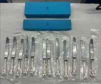Twelve sealed knives laid out with two Birks blue boxes