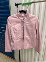 Front view of pink leather jacket on hanger showing ruffle collar, placket and cuffs