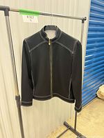 Front view of black jacket on hanger showing zipper and white stitching