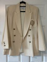 Front view of cream wool blazer hanging, showing double-breasted buttons and crest