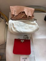 Three bags laid out: pink Calvin Klein, white Coach hobo, red Guess purse