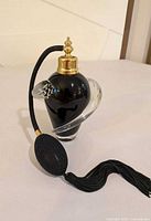 Full view of black handblown glass perfume bottle with clear swirl, gold-tone cap, black atomizer bulb and tassel