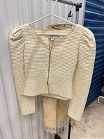 Front view of cream quilted jacket on hanger with gold lace skirt behind