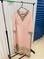 Front view of pink gown on hanger showing beaded V-neckline, cuffs and hem